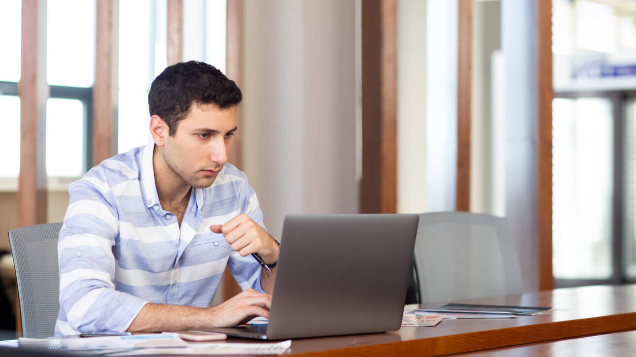 front view young handsome man striped shirt working inside conference hall using his silver laptop daytime work activity building scaled 1