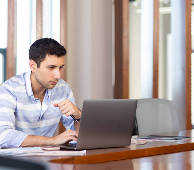 front view young handsome man striped shirt working inside conference hall using his silver laptop daytime work activity building scaled 1